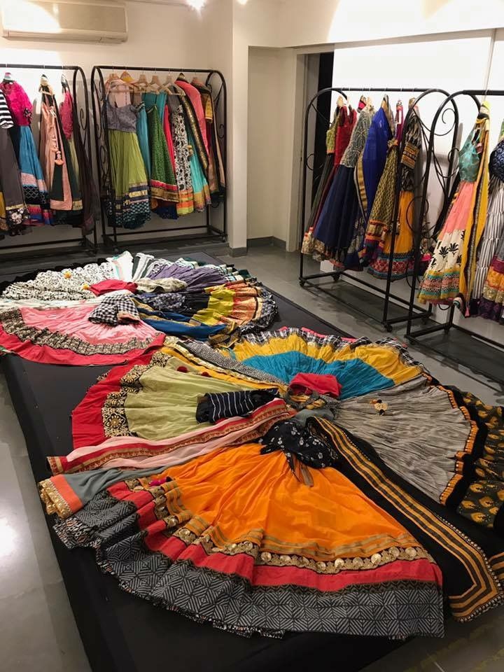 the image showcases a retail setting with a variety of colorful lehengas and dresses. some garments are displayed on hangers along clothing racks, while others are arranged on a large surface, possibly a table or a platform, to showcase the full skirt spread of the lehengas. the fabrics and designs appear to be of indian traditional fashion, featuring vibrant colors and intricate patterns.