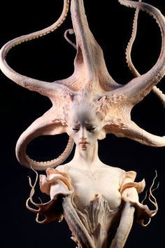 the image showcases a meticulously crafted sculpture of a woman with an octopus forming her hair and upper torso. the creature's tentacles curl intricately around her head, creating an elaborate headdress. the woman's expression is serene, her eyes downcast, and her hands delicately positioned on her chest. the sculpture is rendered in a lifelike pale tone, highlighting the artist's attention to detail and anatomical accuracy.