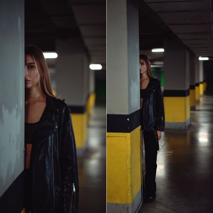 a young woman is standing in a parking garage. she is wearing a black leather jacket and has long blonde hair. she is looking seriously at the camera. the garage is dark and concrete. the walls are yellow and black. the woman is leaning against a yellow wall. the photo is taken from a low angle. the woman is the only subject in the photo. she is wearing black pants under her jacket.