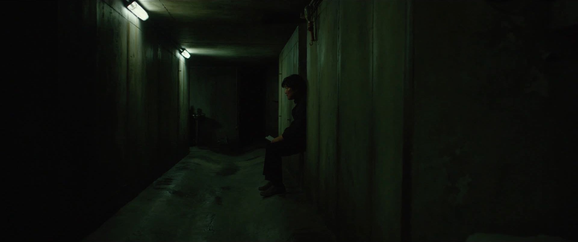 a man sits alone in a dark, concrete tunnel.  he is illuminated by a dim light coming from the end of the tunnel.  the walls of the tunnel are rough and textured. the image is dark and moody, and creates a sense of isolation and loneliness.