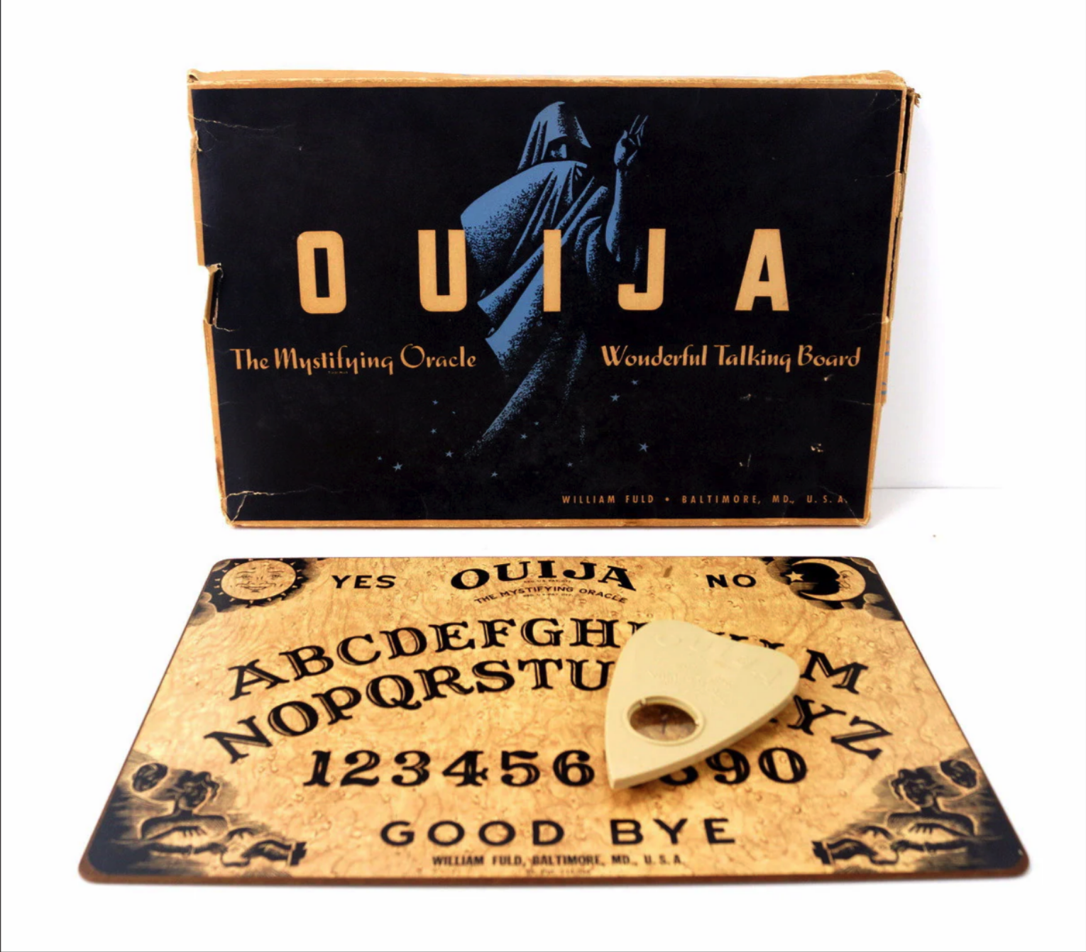 an image of an antique ouija board game. the board itself is wooden with a brown woodgrain pattern. it contains all the letters of the alphabet, numbers 19 and 0, along with the words "yes", "no" and "goodbye".  there is a heart shaped planchette on top of the board.  behind the board is a box with an image of a hooded figure and the text "ouija, the mystifying oracle" and "wonderful talking board."
