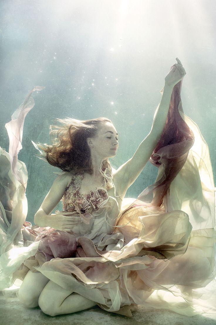 a beautiful woman is submerged in water wearing a flowing gown. the dress is billowing around her, mimicking the movement of the water. her hair is flowing behind her, and she looks ethereal and dreamlike. the lighting is soft and natural, and the colors are muted and calming.