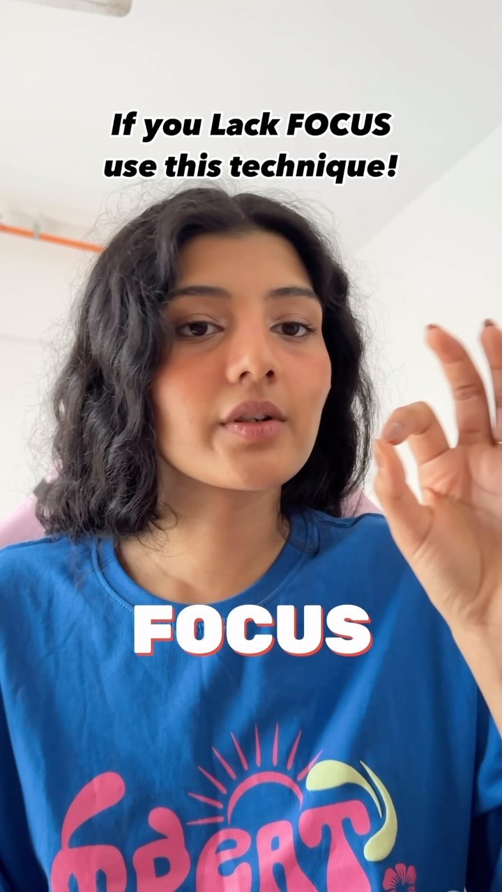 a closeup video captures a young woman with curly brown hair, wearing a bright blue sweatshirt.  she's making an "ok" hand gesture while speaking directly to the camera. text overlays on the video proclaim "if you lack focus use this technique!" and "focus" in large font. the background is a blurred, simple indoor setting.  the overall vibe is one of a helpful, informal selfhelp video offering advice on improving focus and concentration.