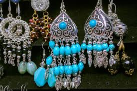 the image shows a closeup view of several pairs of earrings hanging on display, likely for sale. the earrings are a variety of styles, all featuring intricate designs and colorful beads. some earrings are silver with turquoise stones, while others have a more vintage or ethnic look. they appear to be handcrafted and showcase a bohemian aesthetic.