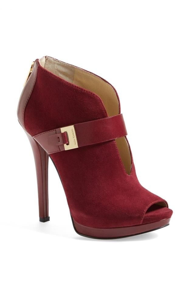 a pair of red suede stiletto peep toe heeled booties. they have a gold buckle on the ankle strap. the shoe has a high heel and a pointed toe. the heel is very high and thin. the shoe is a beautiful color and style.