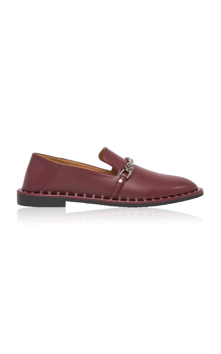 a pair of women's burgundy leather loafers are shown. the loafers have a pointed toe and are adorned with a silver chain detail and studs along the sole. they are slipon style and appear to be made of highquality leather.  the shoes are presented against a plain white background.