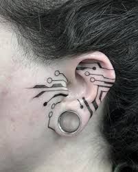 a closeup image shows a person's ear with a unique tattoo design. the tattoo, done in black ink, resembles a circuit board pattern, with lines and small circles that mimic electronic components. the tattoo extends onto the side of the face near the ear. additionally, the ear is stretched with a large gauge earring in the lobe, which gives it a hole. the person's hair is visible above and behind the ear, appearing dark.