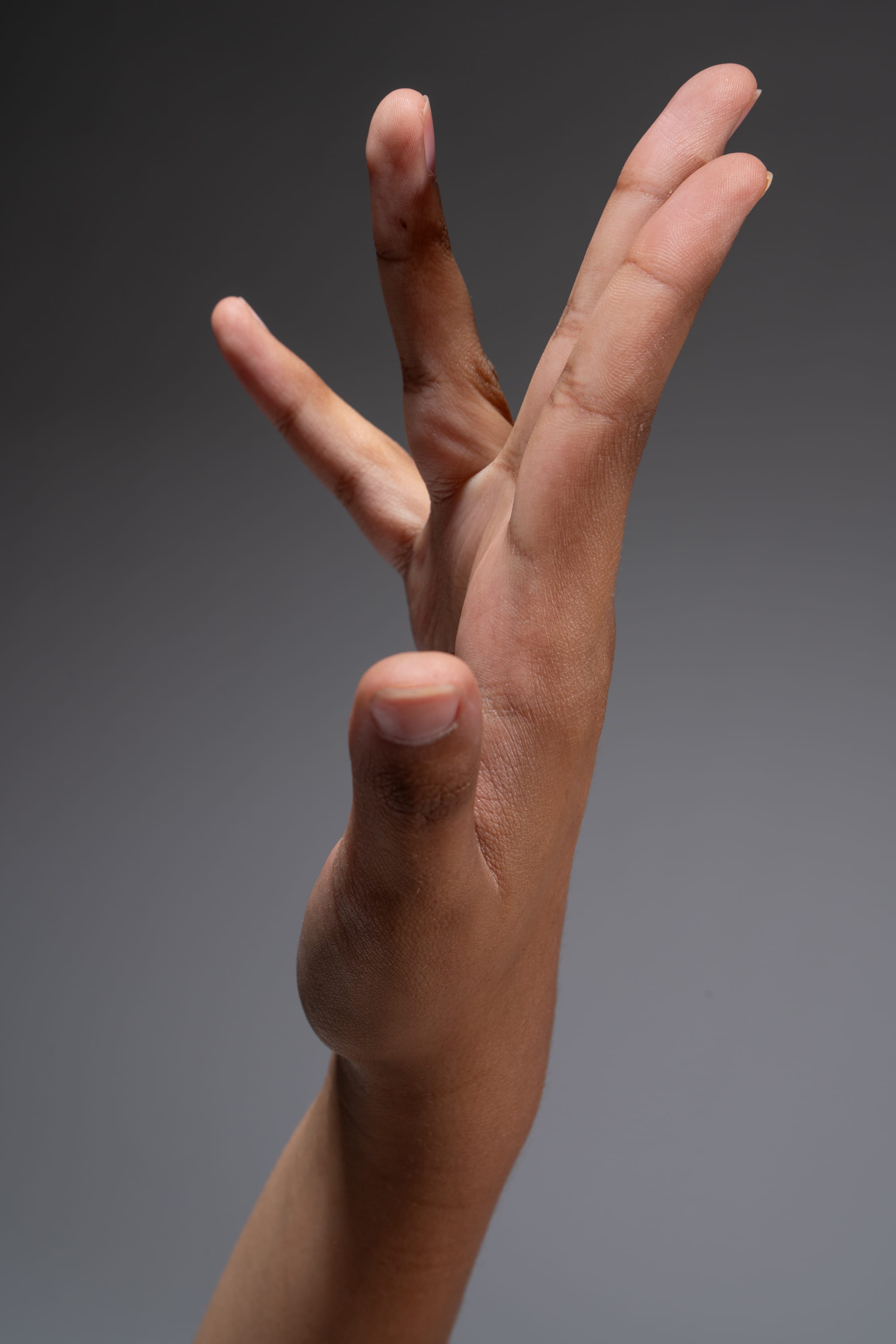 a closeup side view of a person's hand and arm extended upward with an open palm against a solid gray background.