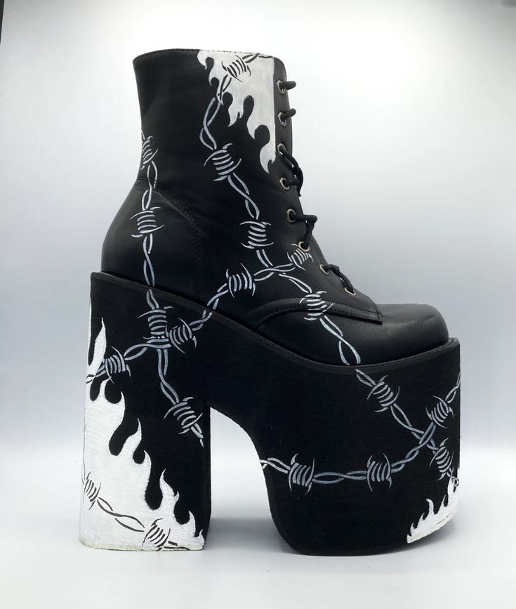 the image shows a black goth platform boot with white barbed wire and fire designs. the boot has a high heel and is laced up.