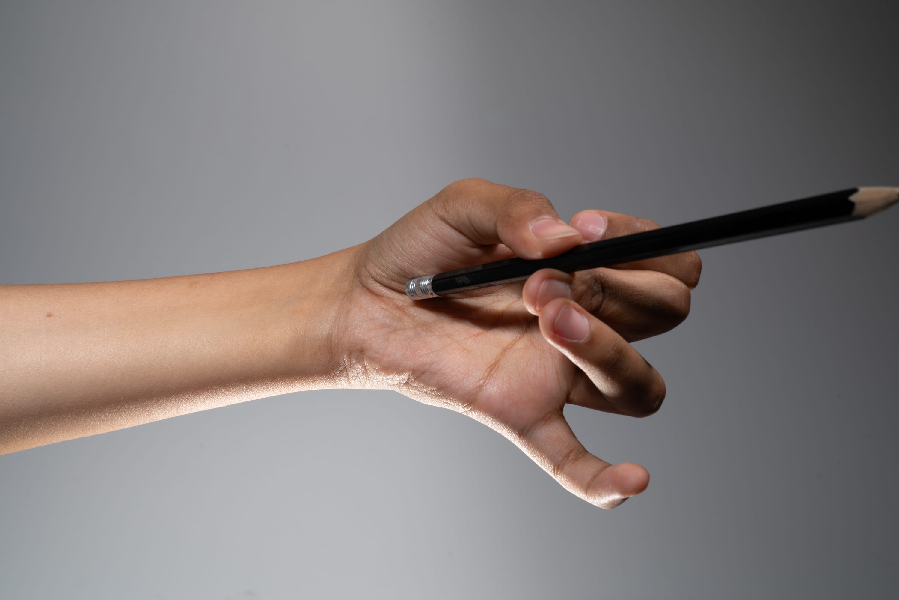 a hand is holding a pencil with the eraser side facing outwards. the hand is extended forward against a light gray background.