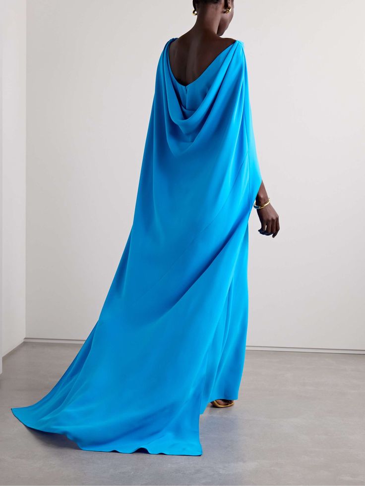 a woman wearing a beautiful long, flowing blue silk gown with a draped back and a simple, elegant design. the gown is a sophisticated and stylish choice for a formal occasion. the woman is standing in a studio setting, posing for the camera. she is wearing minimal makeup and her hair is styled in a simple updo. the image has a modern and contemporary feel.