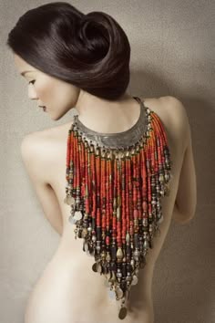 a beautiful woman with her hair up in a bun, wearing a red and silver necklace with a silver pendant. she is looking down with her head tilted. the background is plain and minimalist, allowing the woman and her jewelry to take center stage.