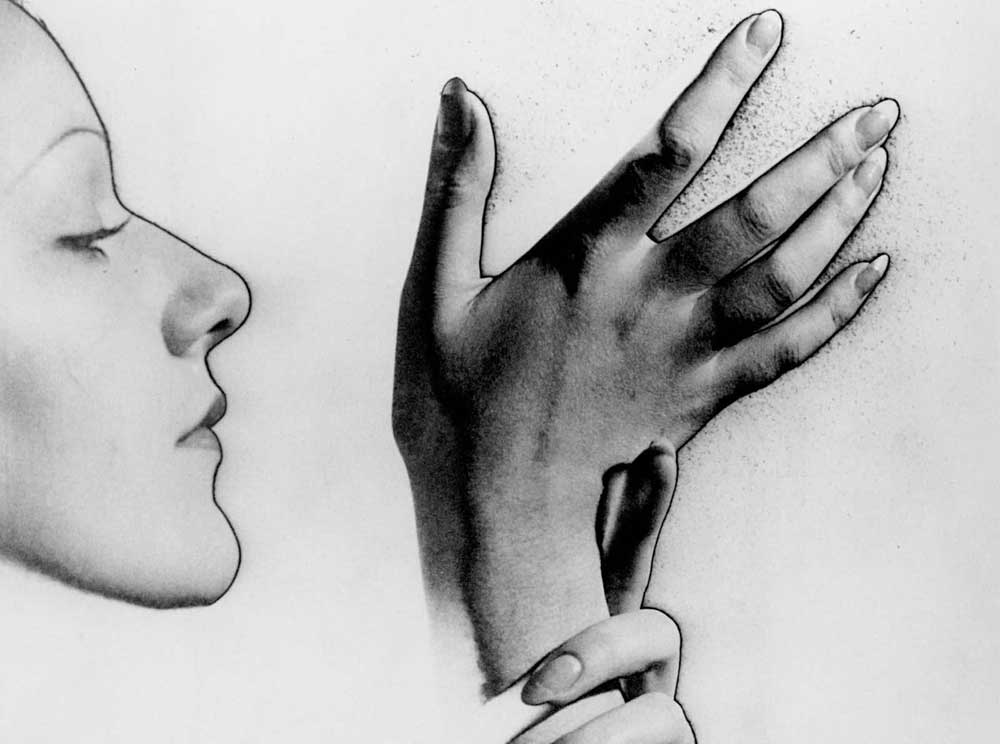 the image is a striking black and white photograph, possibly a surrealist piece.  it features the profile of a woman's face, softly lit and rendered in grayscale, juxtaposed with a dramatically lit, closeup of a hand (seemingly the same woman's) displayed against a textured background. the hand appears almost to be reaching out or exploring, with the fingers gently spread. the contrast between the soft face and the more boldly rendered hand creates a sense of mystery and visual tension. the overall style suggests the work of a skilled photographer focusing on light, shadow, and the interplay of form.  the mood is introspective and somewhat enigmatic.