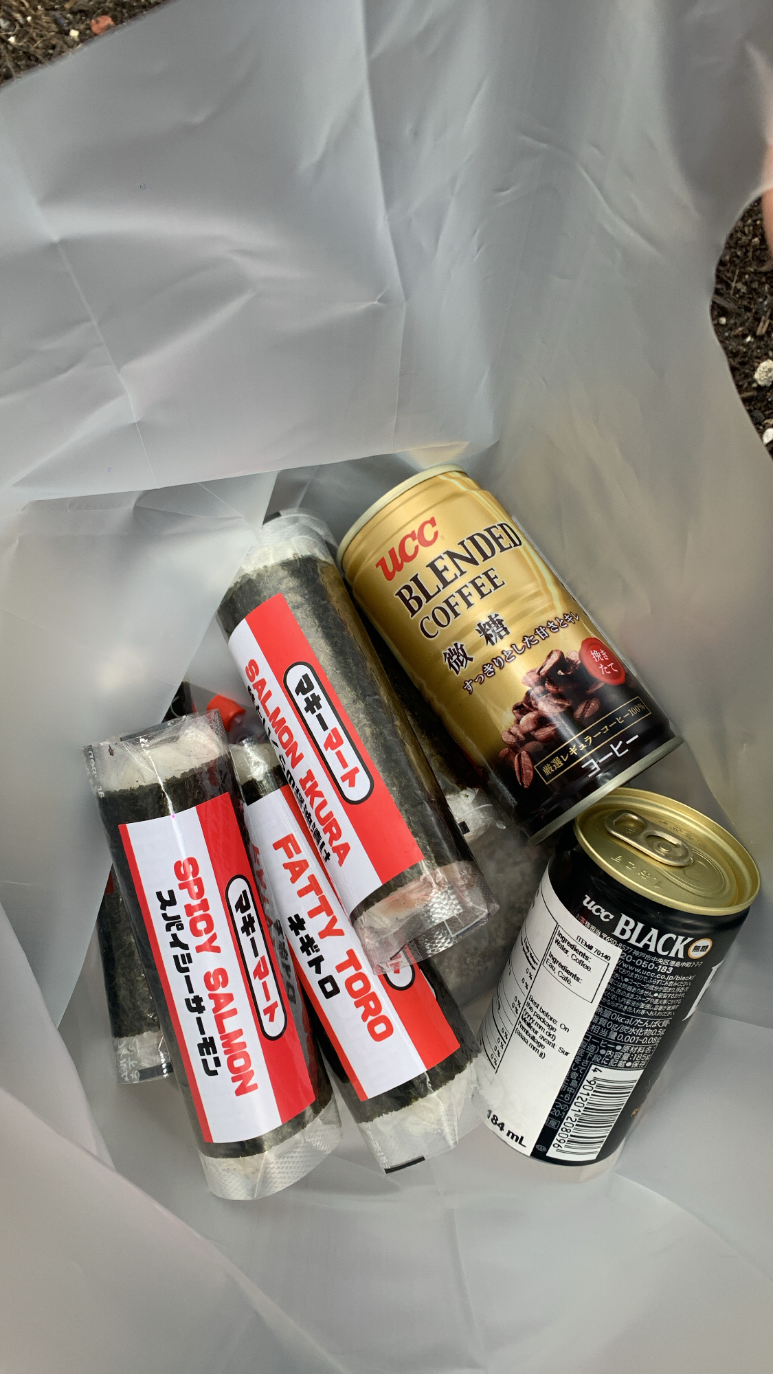 in a white plastic bag are 4 sushi rolls in red and white packaging, a can of ucc black coffee, and a can of ucc blended coffee. the image is taken from a top down view.