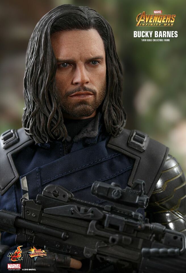 the image is a closeup promotional shot of a highly detailed 1/6 scale collectible figure of bucky barnes (winter soldier) from the movie avengers: infinity war, produced by hot toys. the figure showcases bucky's likeness to actor sebastian stan, complete with his signature long dark hair and facial stubble. he's dressed in his dark blue tactical uniform, featuring his distinctive shoulder armor and prosthetic arm.  bucky is holding a submachine gun with a red dot sight. the background is blurred, focusing attention on the figure itself. the avengers infinity war logo is prominently displayed in the upper right corner, along with the figure's name.  the image likely comes from a product advertisement or promotional material.