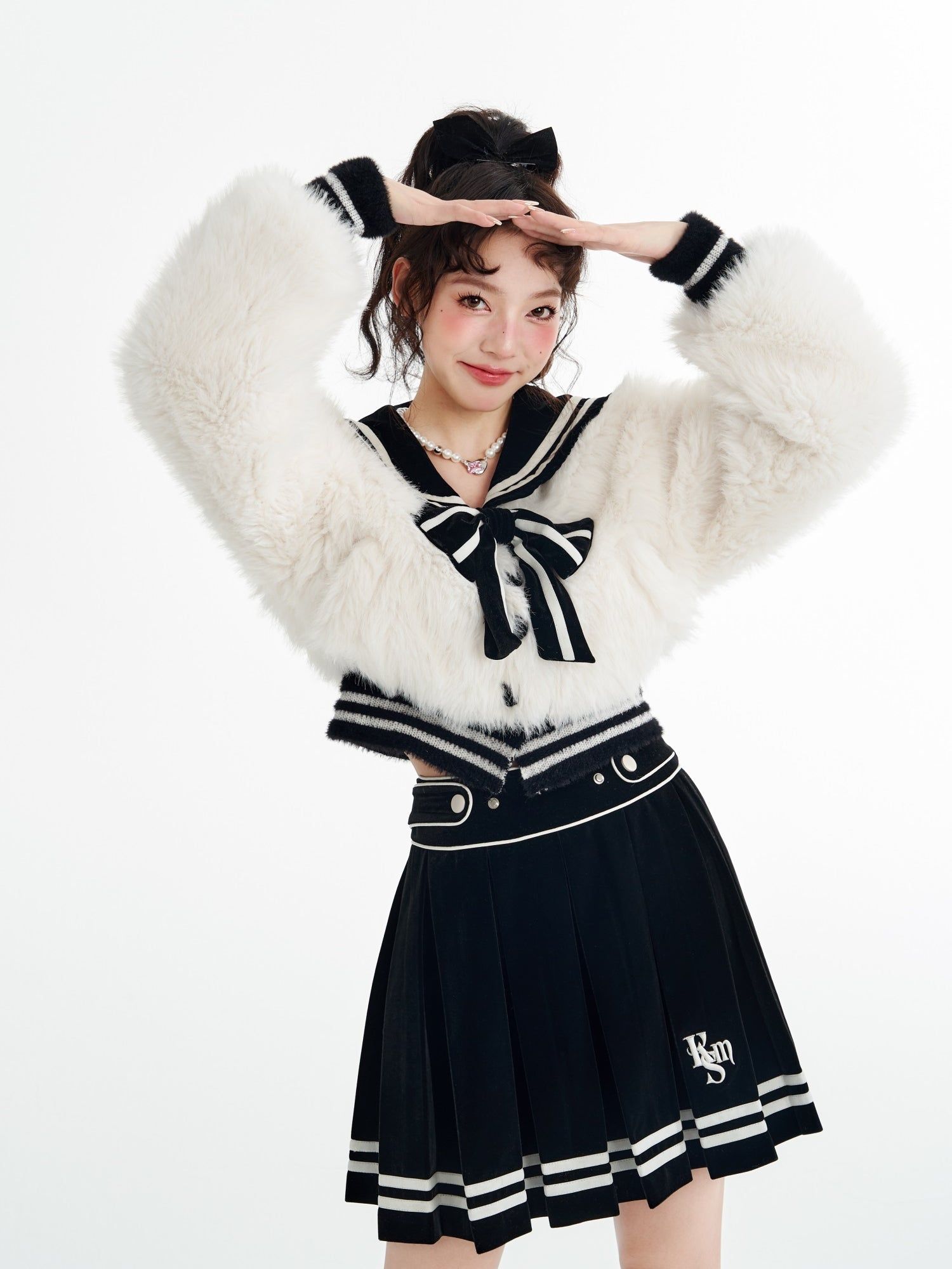 a young asian woman is posing in a studio shot against a white background. she is wearing a stylish and youthful outfit consisting of a white, fluffy fur jacket with a sailor collar and a black bow, paired with a pleated black skirt. her hair is styled up with a black bow. she is smiling and holding her hands up near her forehead. the image conveys a sense of fashion, cuteness, and preppy style.
