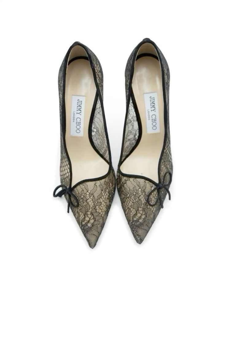 a pair of black lace jimmy choo heels are presented against a white background. the shoes are pointytoed pumps with a delicate lace overlay and small bows at the toes.  the jimmy choo brand label is visible inside each shoe. the image is a clean, product shot showcasing the shoes' details.
