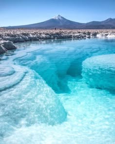 a serene landscape of a sparkling blue lake in front of a snowcapped mountain. the water is crystal clear and reflects the blue sky. the surrounding landscape is a dry, barren desert with a white, saltencrusted surface.
