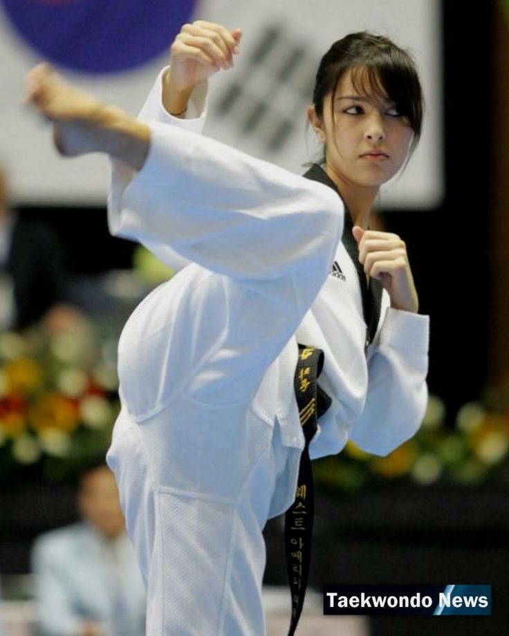 a young woman in a taekwondo uniform, wearing a black belt, performs a powerful kick during a competition. she is dressed in white with a black belt, showcasing her skills and athleticism in this dynamic sport.  the woman is in focus while the background is blurred, highlighting her movement and action. the image captures the essence of taekwondo, its discipline, and its physicality.