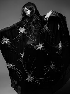 a woman wearing a black star patterned gown poses against a dark background for a fashion shoot.