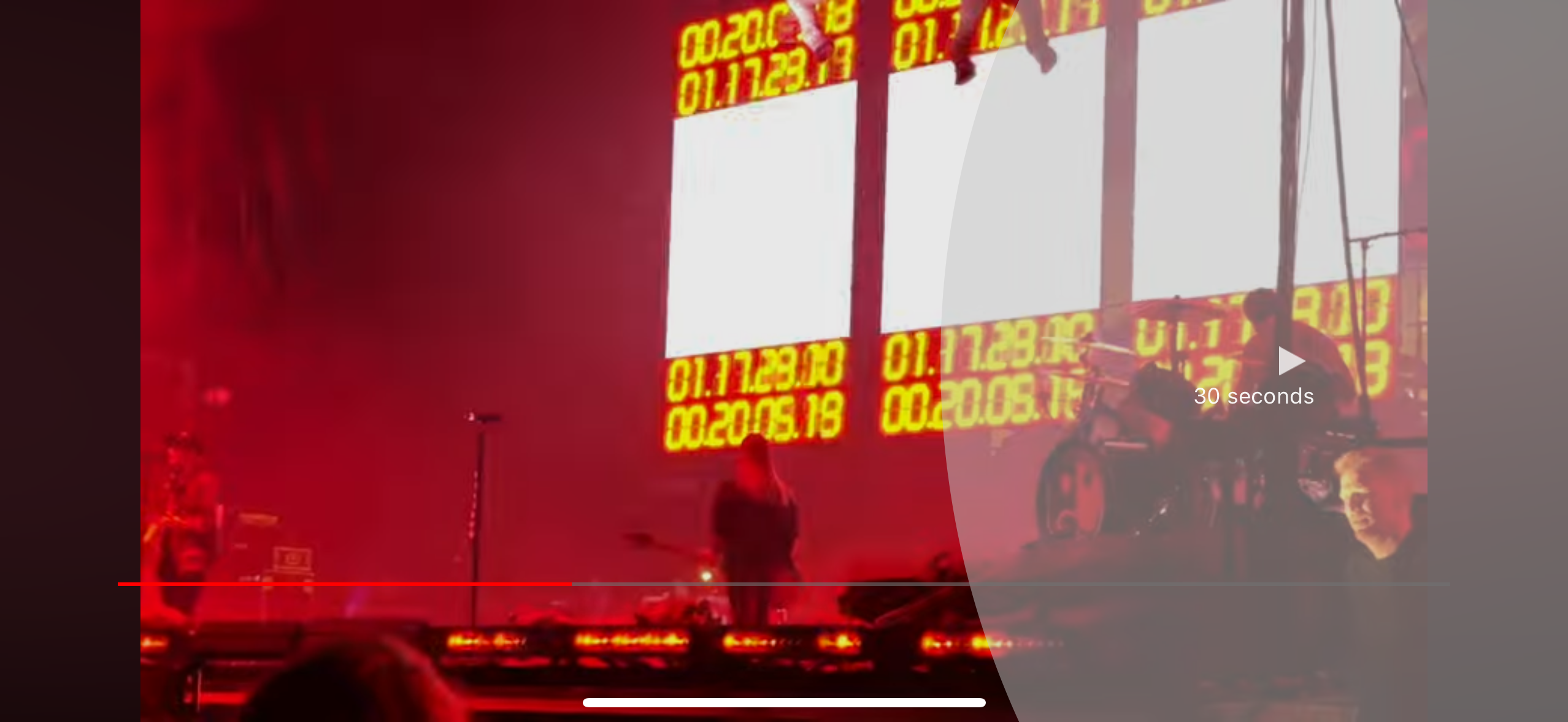 a concert performance taking place on a stage with red lights and a band playing music. the stage is dark and the crowd is excited, and the singer is on stage with a microphone in hand. the band is playing a song and the crowd is cheering, and the atmosphere is electrifying.