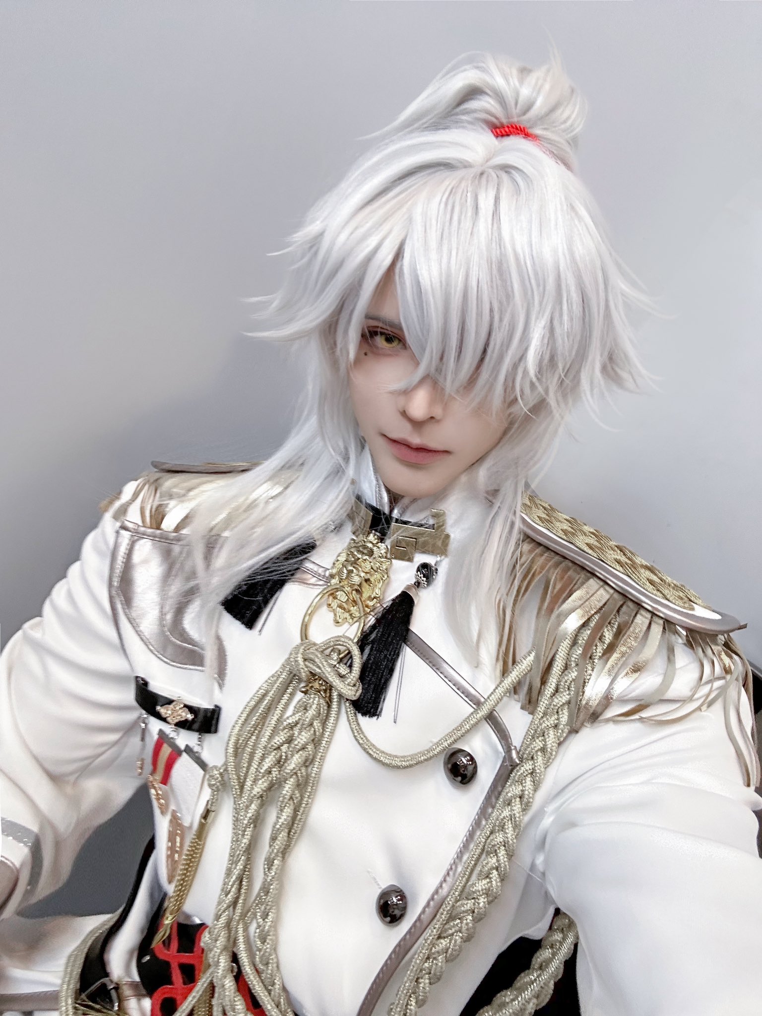 a closeup portrait of a person cosplaying a character with white hair and a white military uniform with gold trim. they are looking down at the camera and have a serious expression on their face.