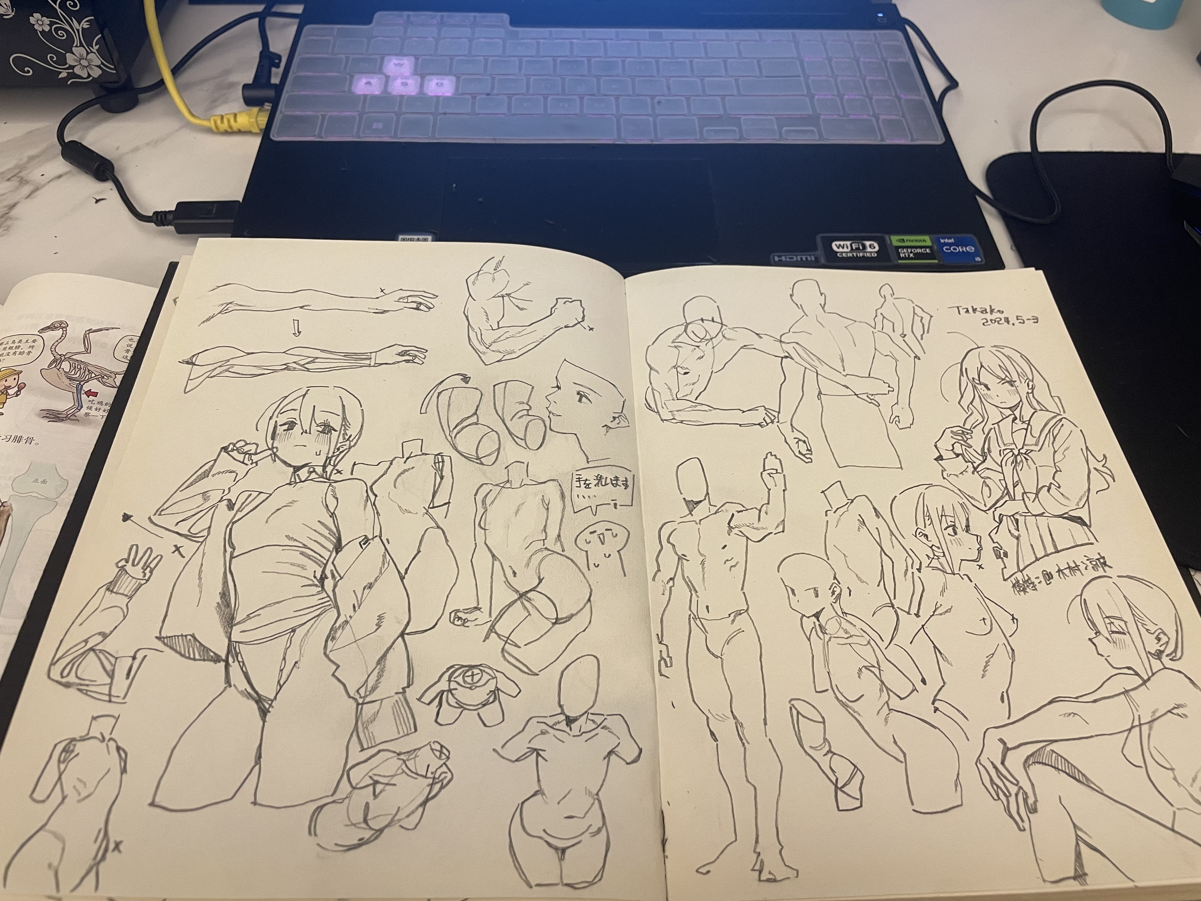 an open sketchbook filled with pencil sketches of various figures, including animestyle characters and anatomical studies. the sketchbook sits on a desk with a laptop in the background.