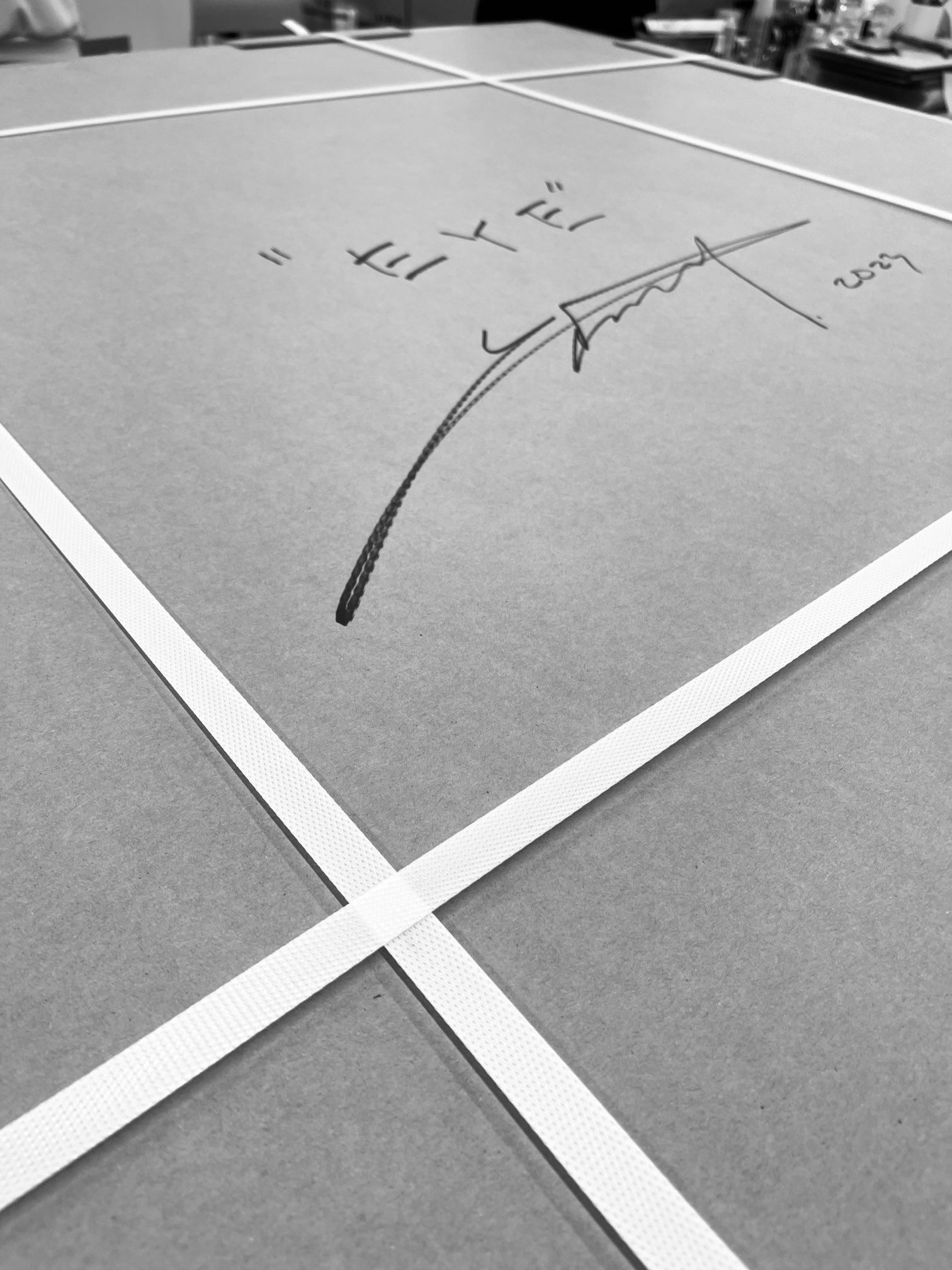 a closeup black and white photo of a cardboard box with packing tape and a signature in marker.