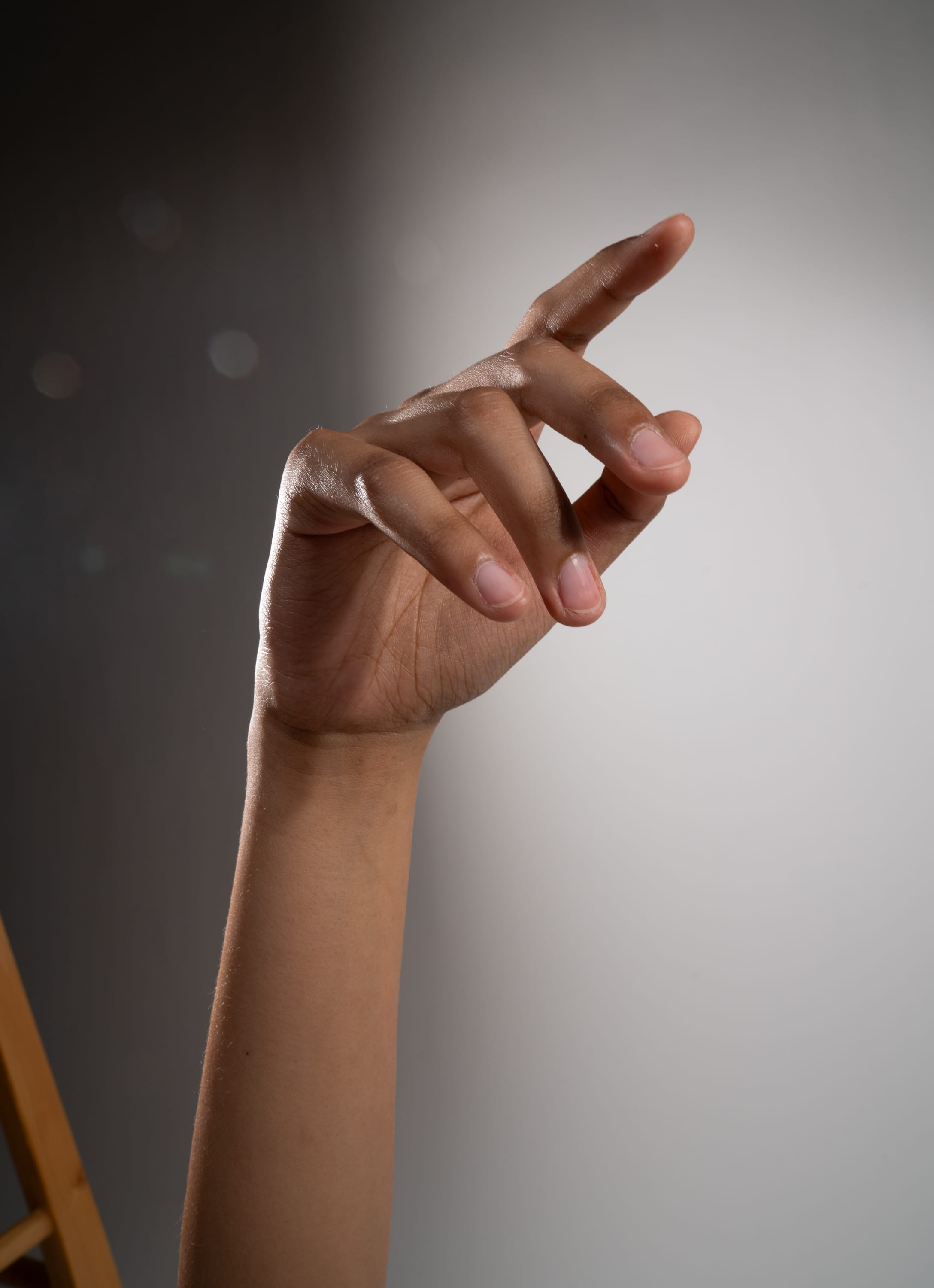 the image shows a closeup of a person's arm and hand extended upward against a gray and white background. the hand is slightly curled, as if reaching or gesturing towards something. the lighting is soft and diffused, highlighting the texture and details of the skin.