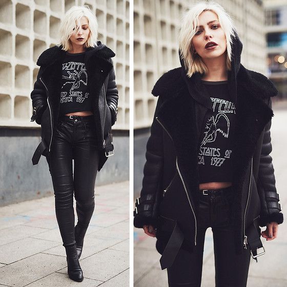 the image shows a stylish blonde woman wearing an allblack outfit.  the central piece is a black sheepskin aviator jacket with a slightly oversized fit. underneath, she's wearing a cropped black band tshirt (with a zeppelin design) and tight black leather pants. she completes the look with black ankle boots. the setting appears to be an urban outdoor area with a modern architectural background. the image is split showing the woman from two slightly different angles. the overall style is edgy, cool, and rock and rollinspired.
