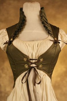 a closeup shot of a mannequin torso wearing a green steampunkinspired corset with a high ruffled collar. the corset is laced up the front with brown ribbon and features brass grommets and eyelets. the mannequin also wears a simple white peasant blouse underneath the corset. the background is a warm brown color.