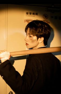 a young asian man with a bruised face is holding a wooden stick.  he is standing in a doorway and illuminated by a spotlight.  the image has a dramatic and mysterious feel to it.