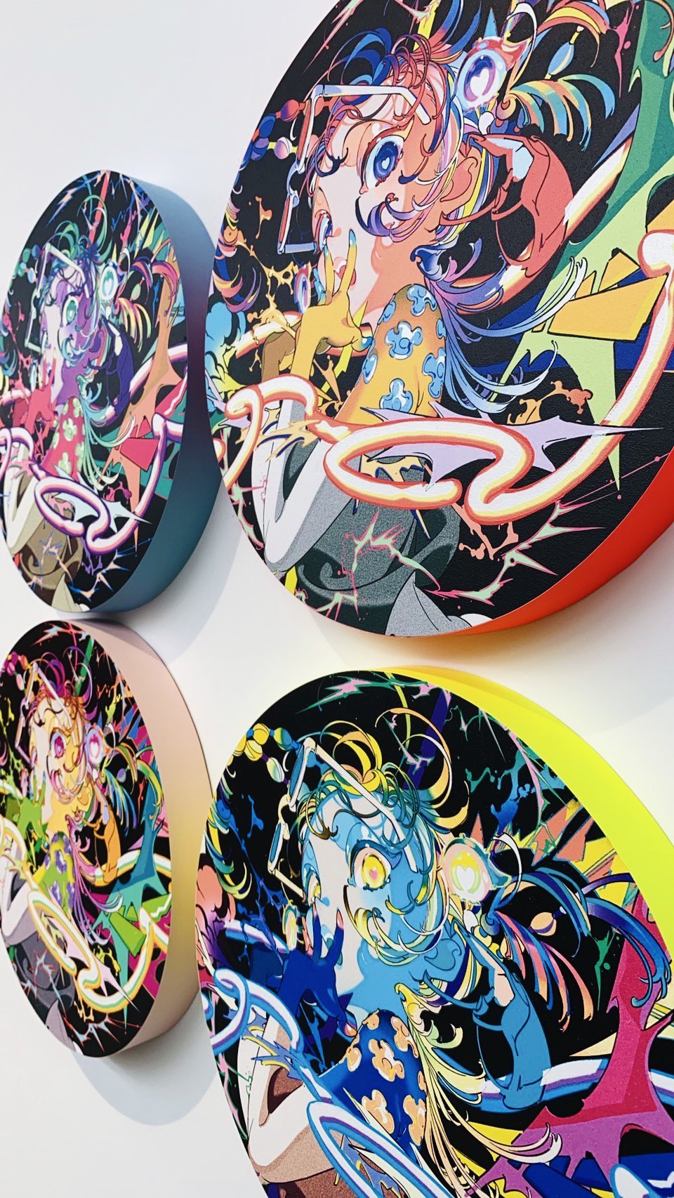 the image showcases four circular art pieces mounted on a white wall. each piece features a vibrant and detailed illustration of an animestyle girl, rendered in a dynamic and colorful popart aesthetic. the girls are depicted with large eyes, flowing hair, and elaborate outfits, set against backgrounds filled with abstract shapes, lightning bolts, and other graphic elements.