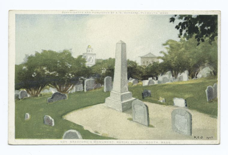 a vintage postcard depicts gov bradford's monument in burial hill, plymouth, massachusetts. the monument is a tall obelisk surrounded by graves, trees, and buildings. the postcard is copyrighted and published by a.s. burbana and marked with "h.c.d 1920".