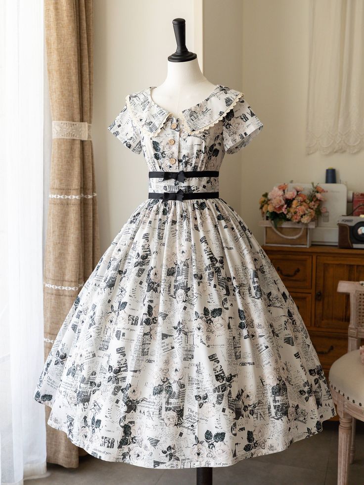 a vintageinspired white dress with a newspaper print and floral accents. the dress has a classic silhouette with a fitted bodice, short sleeves, and a full skirt. it is displayed on a mannequin in a welllit room. the overall style is elegant, feminine, and romantic.