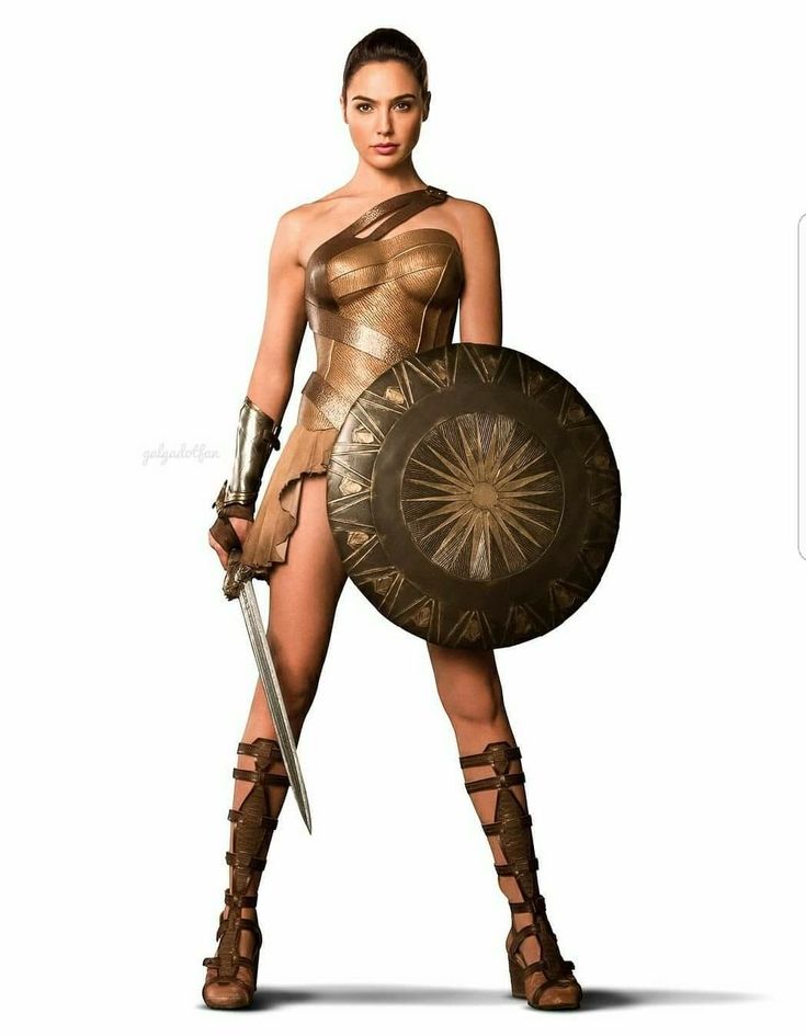 a woman dressed as wonder woman, with a sword in one hand and a shield in the other. she is looking directly at the camera with a serious expression on her face. she is wearing a golden and brown armor, with a skirt and boots. she is standing on a white background.