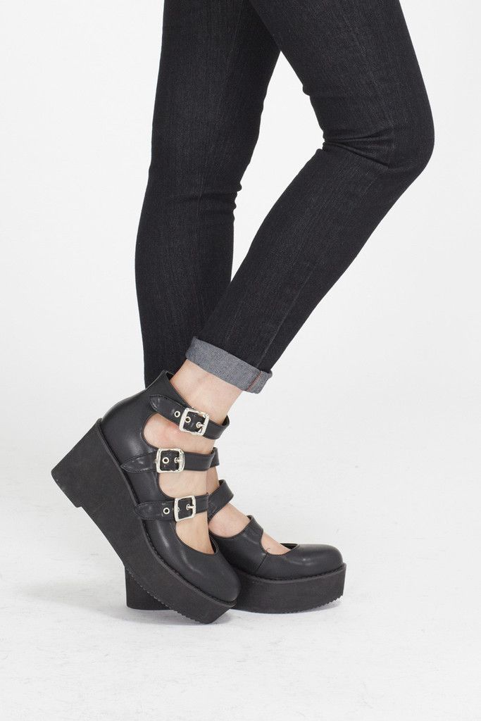 a person is wearing black, platform mary jane shoes with three straps and buckle closures. they are also wearing dark denim, skinny jeans that are cuffed at the ankle. the background is plain white.