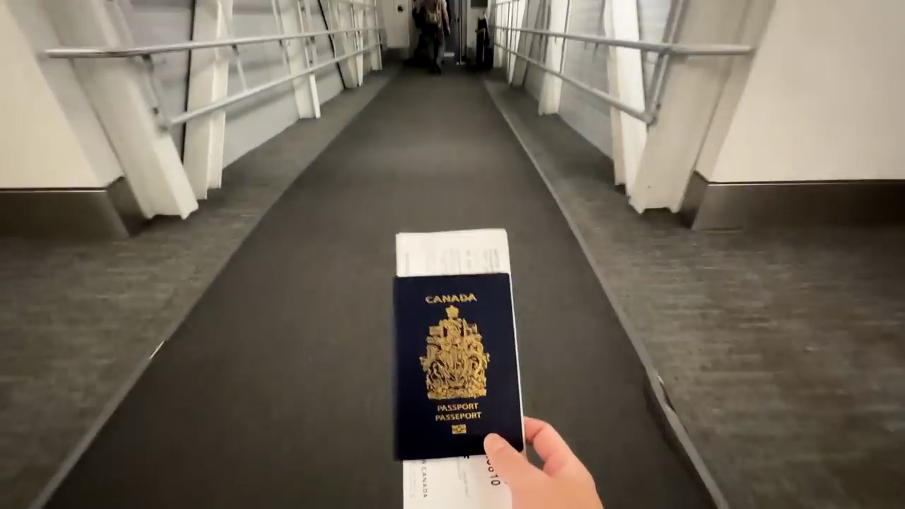 a firstperson perspective shot inside an airport jet bridge. a hand holds a canadian passport and boarding pass, suggesting the individual is about to board a plane. the environment is brightly lit with artificial light, and the walkway is empty except for a person walking in the distance. the overall atmosphere suggests anticipation and the start of a journey.