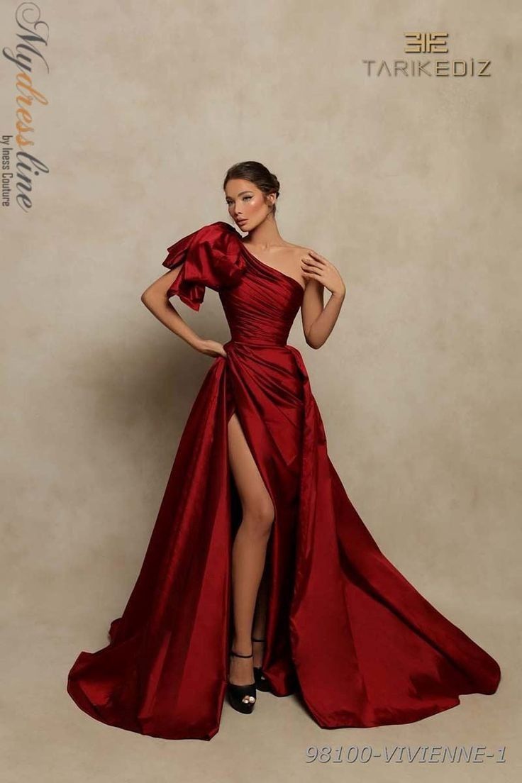 a woman in a stunning red gown stands against a neutral backdrop. the dress is a long, flowing gown with a oneshoulder design and a high slit. the dress is made of luxurious silk fabric, with an elegant and glamorous look. the woman's makeup is natural and radiant, and her hair is styled in a simple updo. she exudes confidence and elegance, showcasing a classic and timeless fashion sense. the background is simple and neutral, allowing the dress to take center stage.  the designer,  tarikediz, is known for his exquisite designs and attention to detail, creating a dress that truly stands out as a piece of art.
