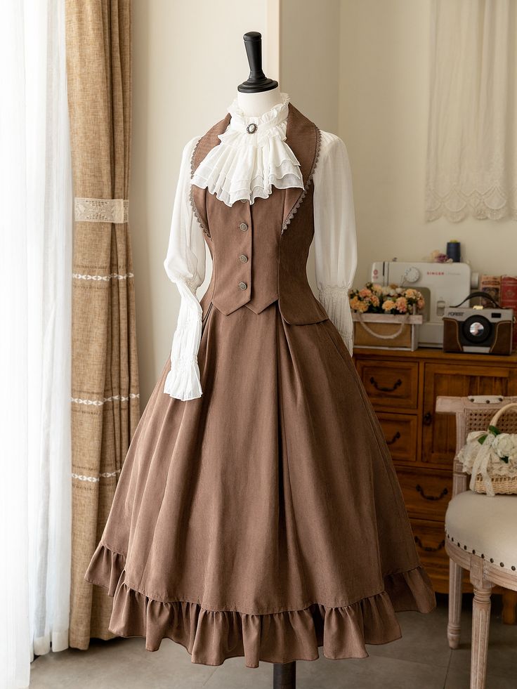 a brown vintage style lolita fashion dress displayed on a mannequin. the dress is brown and has a long, full skirt, a fitted bodice with a vest. the dress is shown with a white blouse with a large collar underneath. the dress is in a room with white walls and lace curtains. there is a wooden cabinet and a chair in the background.