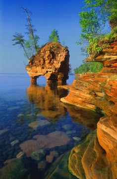 a scenic view of a rocky cliff that rises up out of the water, creating an island.  the cliff is a vibrant orange and red and is surrounded by sparkling turquoise water. the background is a clear blue sky with a few small clouds. the image is taken from the shoreline, looking out at the island.  the photo captures the beauty of nature and the peaceful tranquility of the island.  it is a perfect example of how nature's beauty can be aweinspiring.