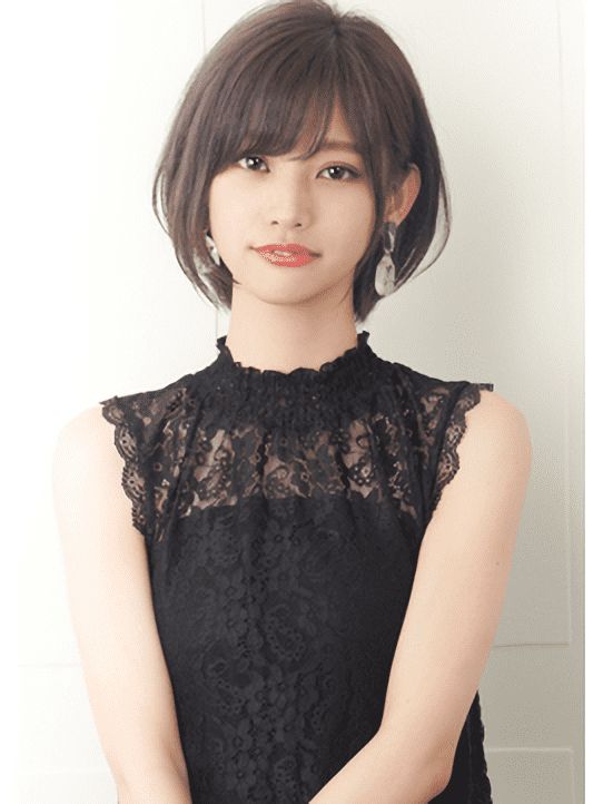 a young asian woman with short black hair, bangs, and earrings smiles at the camera. she is wearing a black lace dress and has a beautiful, classy style. the background is a white wall.