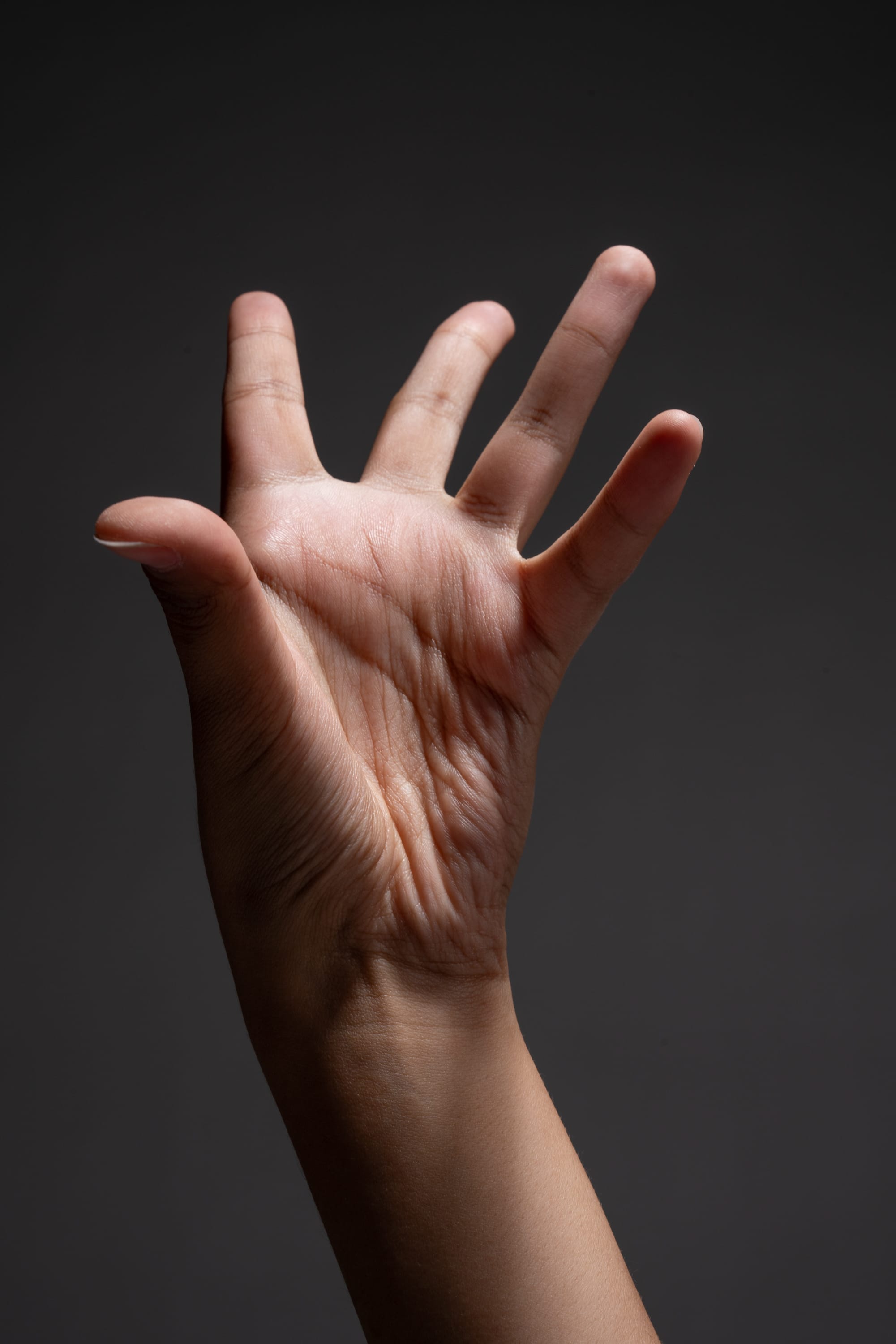 a closeup of a hand reaching upward against a dark gray background. the studio lighting accentuates the wrinkles and texture of the skin.