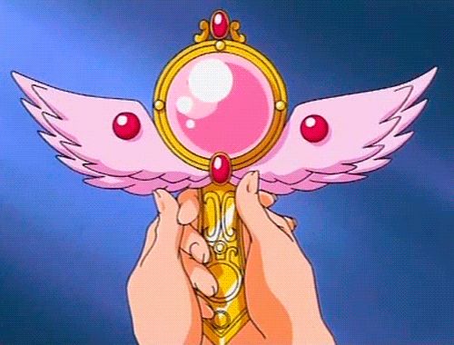 the image depicts a pair of hands holding a magical staff with pink wings and a large pink orb in the center, reminiscent of the eternal tiare from sailor moon.