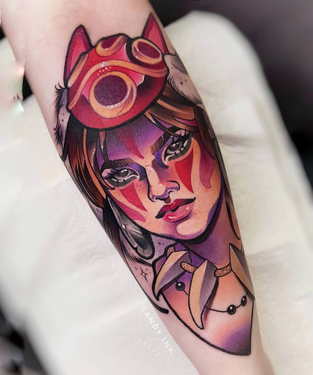 a closeup shot of a forearm tattoo of princess mononoke from the studio ghibli film of the same name. the tattoo is in a neotraditional style with bold lines and vibrant colors. the character is depicted in a portrait style, with her head and shoulders visible. she is wearing her signature mask and has a determined expression on her face. the tattoo is set against the backdrop of the person's skin. the lighting is bright and even, highlighting the details of the tattoo.