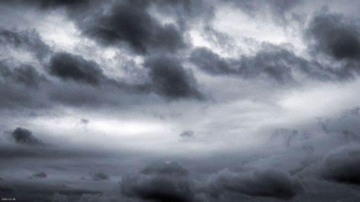 this image is a closeup of a dark, overcast sky filled with thick, gray clouds. the light is dim, casting a moody and atmospheric feeling. the clouds appear heavy and ominous, giving the impression of an impending storm.