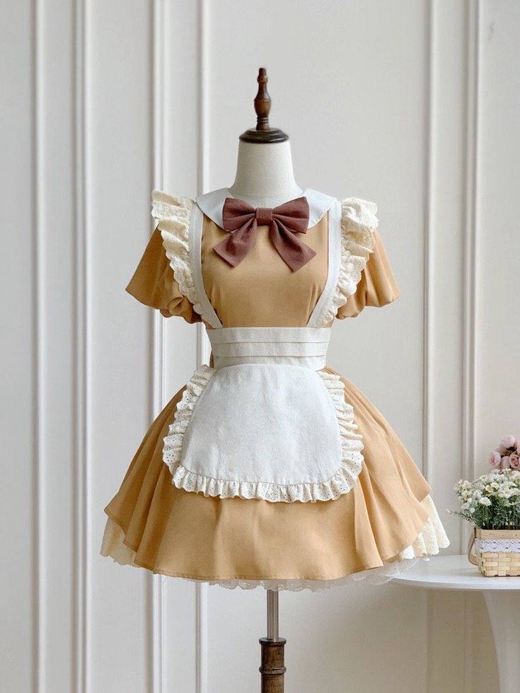 a honeygold maid dress is displayed on a mannequin against a white studio backdrop. the dress features a classic silhouette with a square neckline, puffed sleeves, and a full skirt adorned with ruffles and lace trim. a crisp white apron with lace detailing and a matching bow tie completes the charming look.
