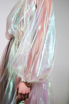 a closeup of a woman's arm, wearing a sheer, iridescent dress. the fabric is flowing and has a pastel, dreamlike quality. the woman's hand is visible, clutching the fabric.  the image is ethereal and elegant, highlighting the delicate beauty of the dress and the woman's arm.