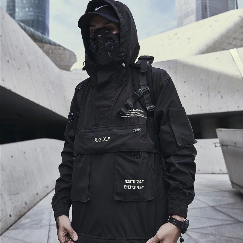a man in a black hooded jacket with a mask is standing in a city. he is looking to the side, and his jacket has multiple pockets and straps.