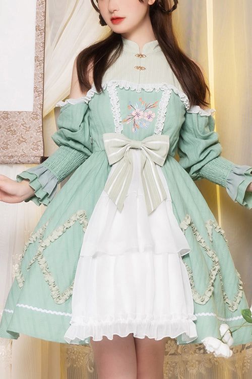 a woman is wearing a green and white lolita dress with floral embroidery. she is posing in a studio setting.